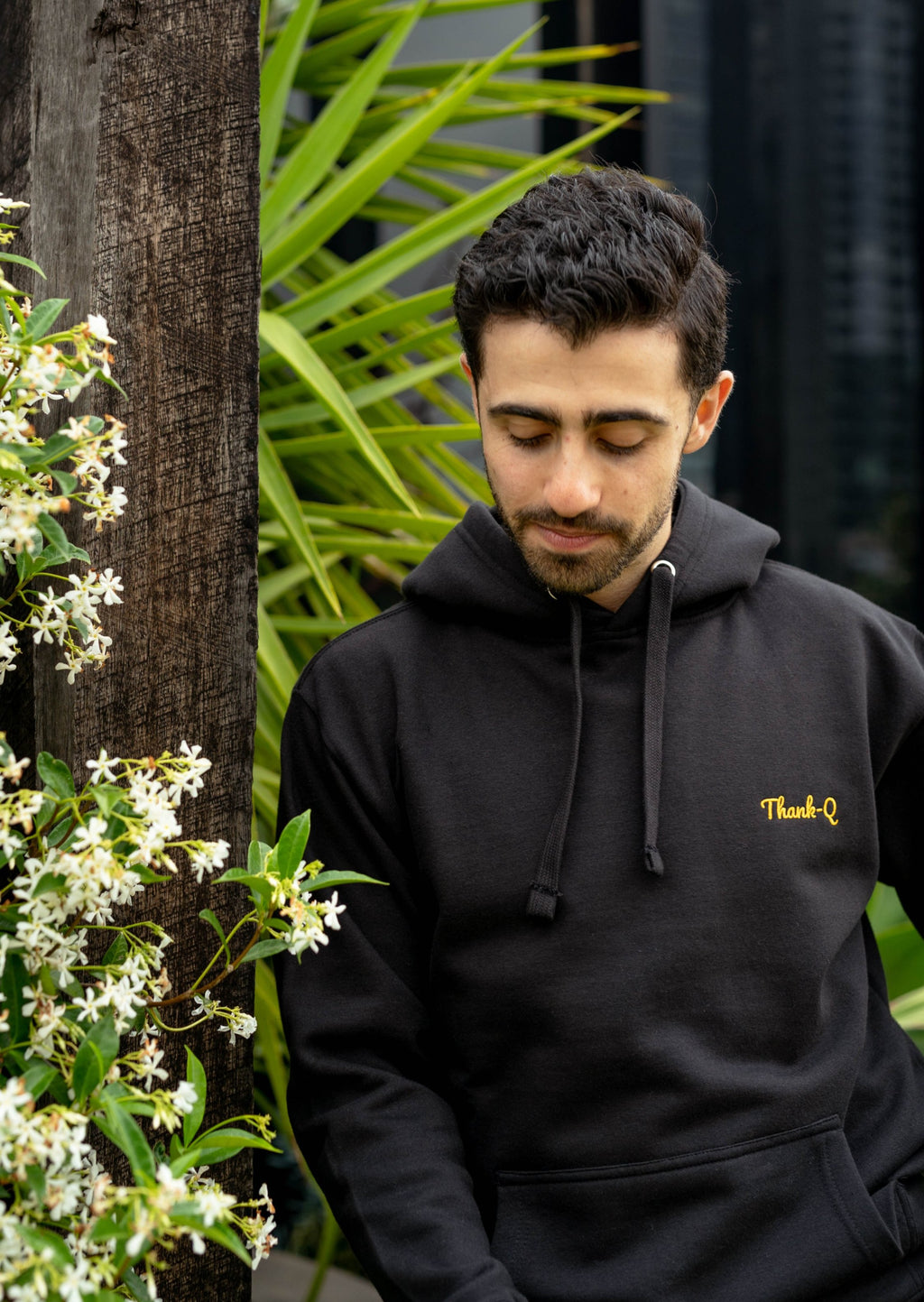 darren posing black thank-q embroidered hoodie in bushes